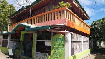 Experience the vibrant atmosphere of this two-story building, featuring a covered area with a signboard showcasing local offerings and a balcony with a railing overlooking the surrounding trees.