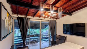 Una habitación moderna con un amplio ventanal corredero, una mesa blanca, sillas de cuero negro y un televisor de pantalla plana montado en la pared.
