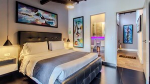 Una habitación de hotel moderna con una cama grande, cabecera, mesitas de noche y obras de arte en las paredes.