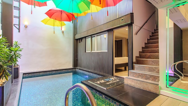 Una piscina con suelo de baldosas, una escalera y coloridos paraguas colgando del techo.