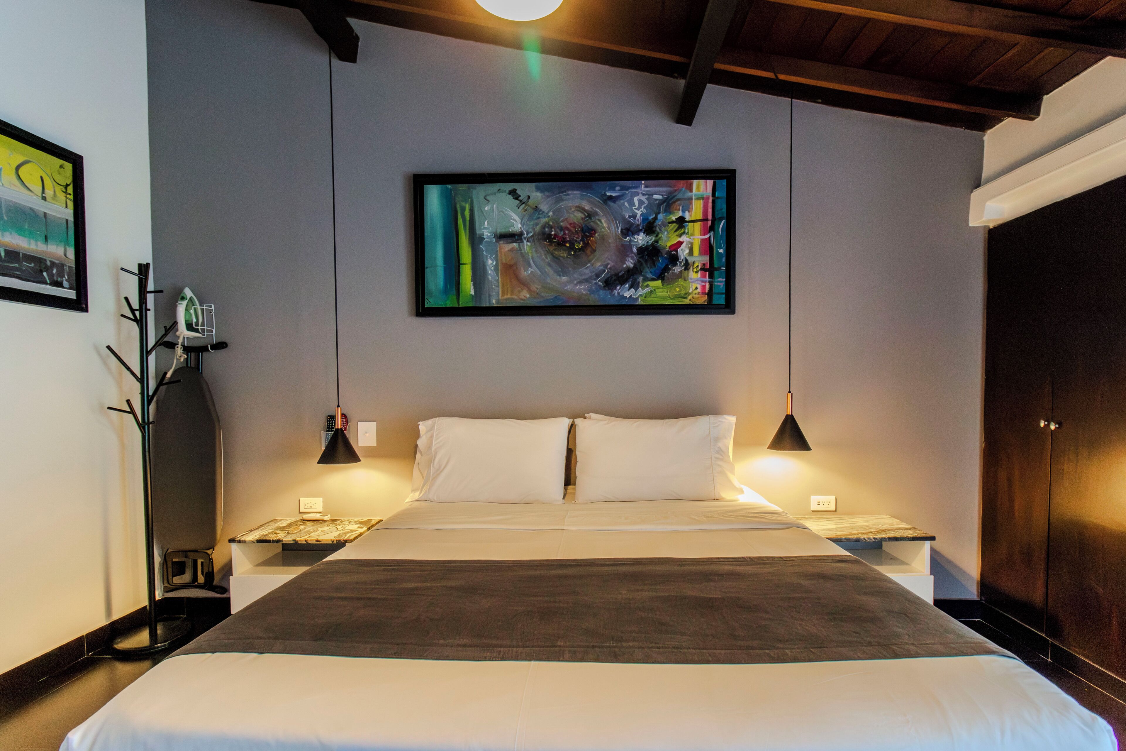 A hotel room with a large bed, two bedside tables, a wall-mounted painting, and a wardrobe.
