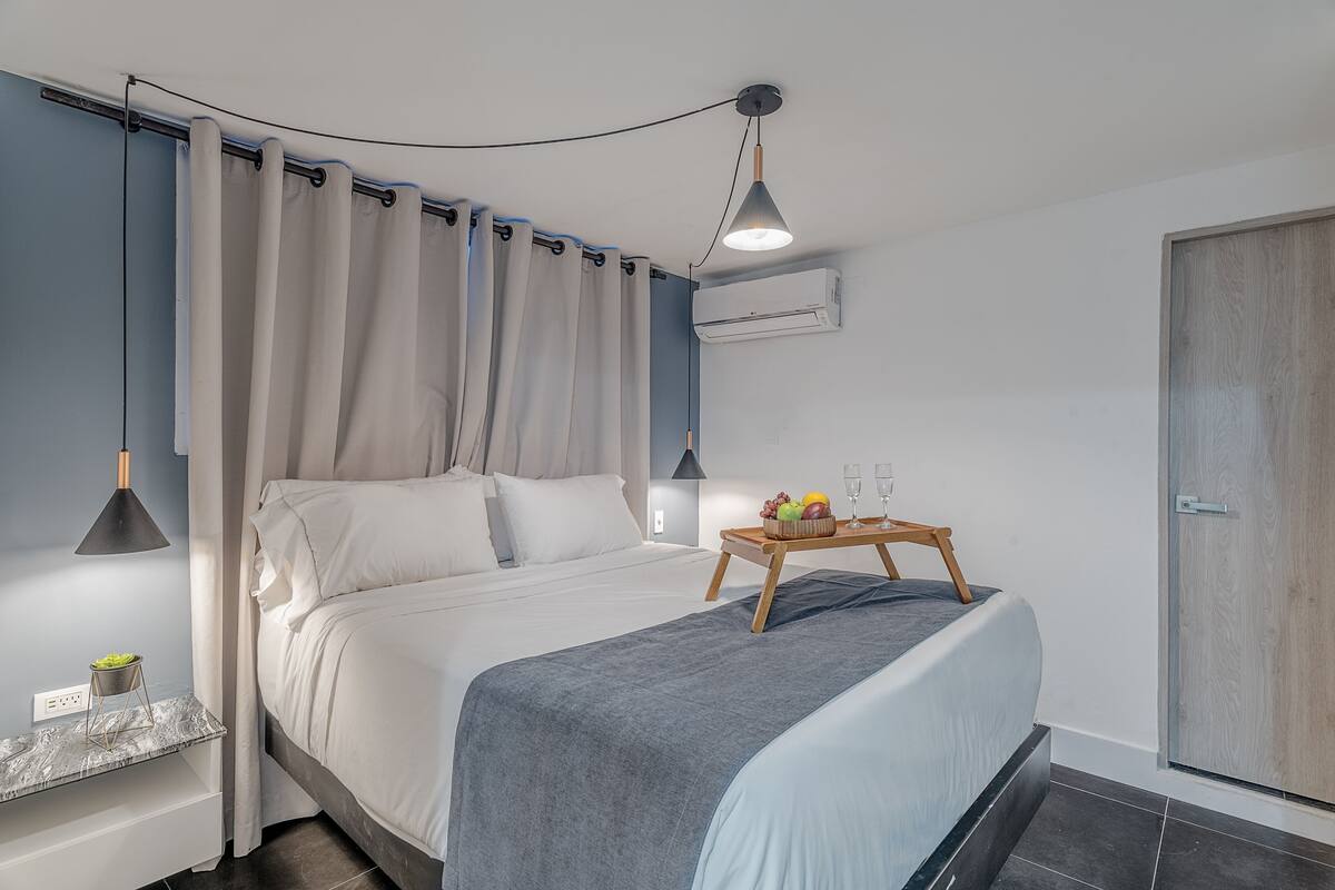 Un dormitorio moderno con cama, mesita de noche y una bandeja con frutas y vasos.