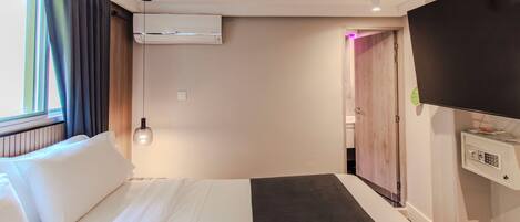 A hotel room with a bed, an air conditioning unit, a television, and a door leading to another room.