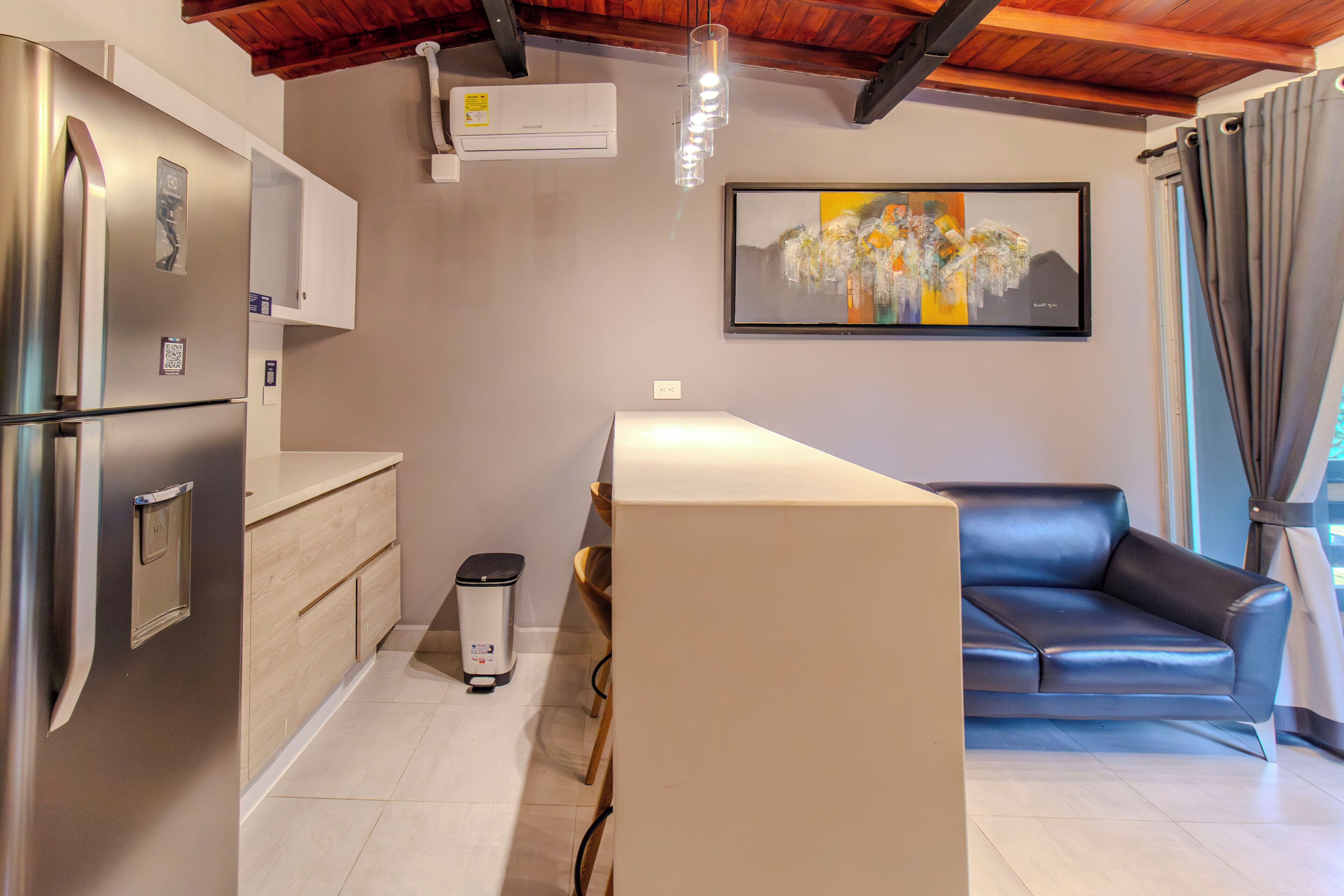 A compact kitchen with a refrigerator, a trash bin, and a sofa.