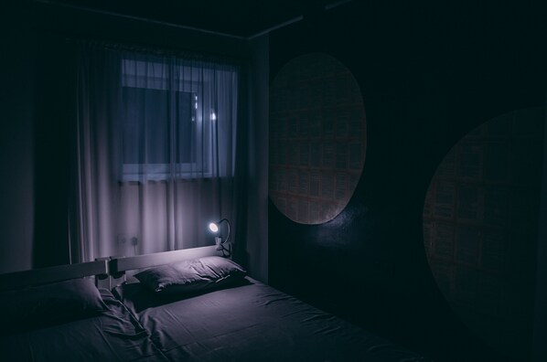 A dimly lit room with a bed, a window with curtains, and a round wall feature.