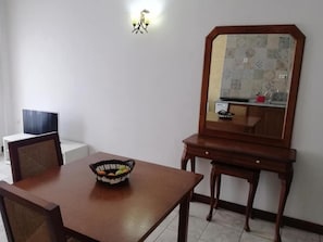 A dining area with a wooden table, chairs, a fruit basket, a television, and a mirror with a patterned backsplash. - Hotel Al Andalus (Torrox)