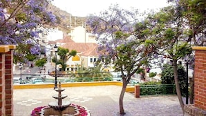 A courtyard with a fountain, surrounded by brick walls and trees with purple flowers. - Hotel Al Andalus (Torrox)