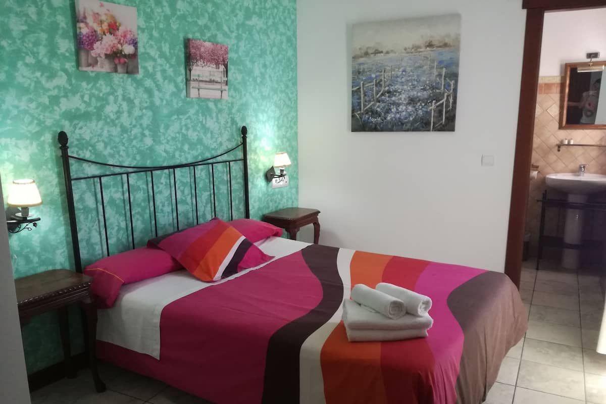 A bed with a colorful bedspread, a nightstand with a lamp, and a painting on the wall.