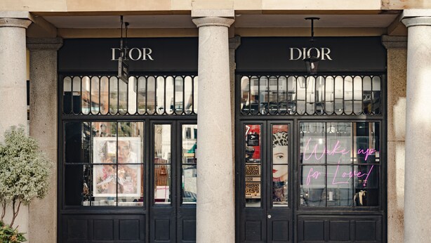 Vitrine com duas portas pretas grandes com a inscrição "Dior" e um letreiro de neon que diz "Maquiagem por Amor!"