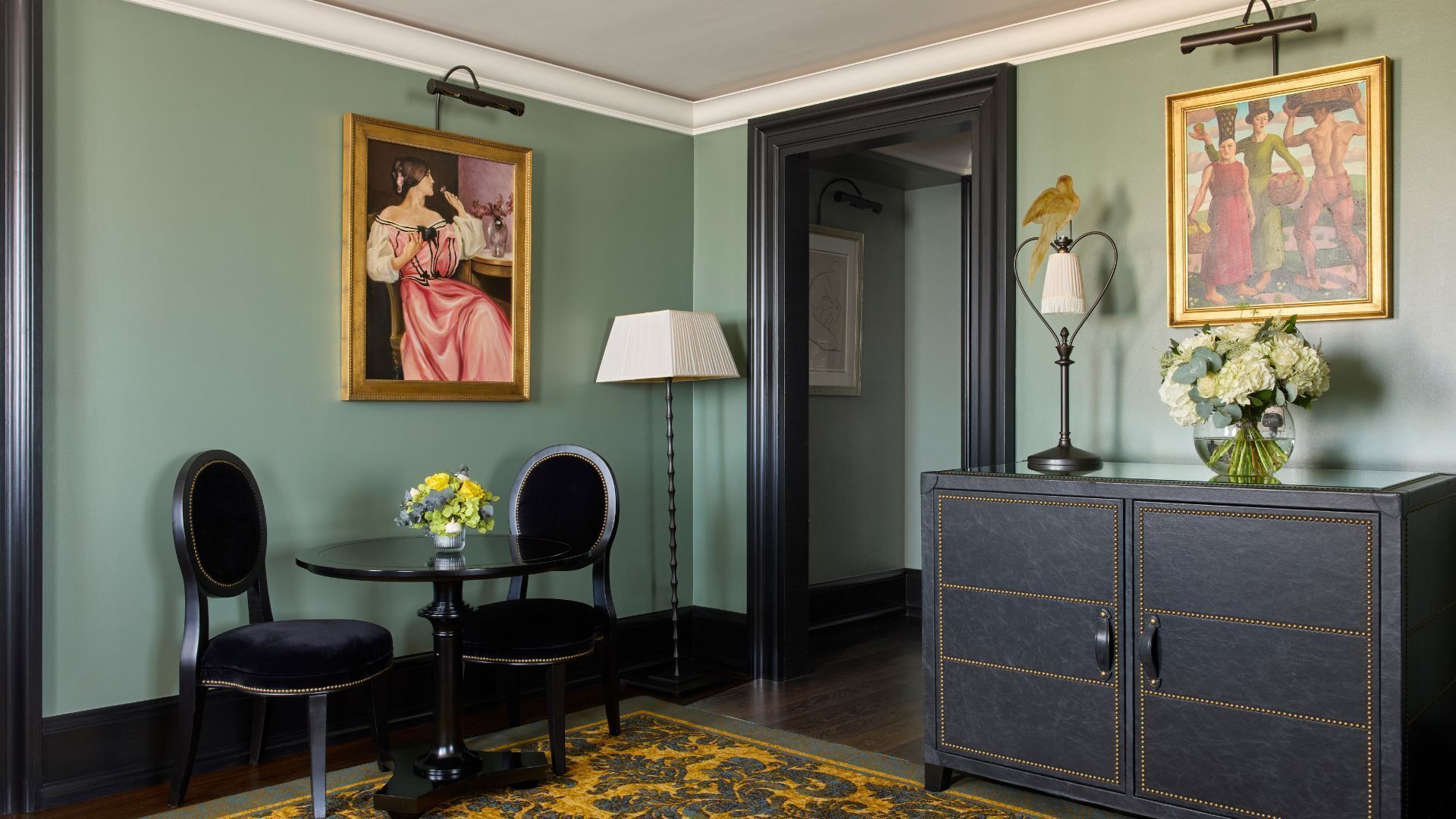 A room with a dark wooden cabinet, a painting, a lamp, and a table with chairs.