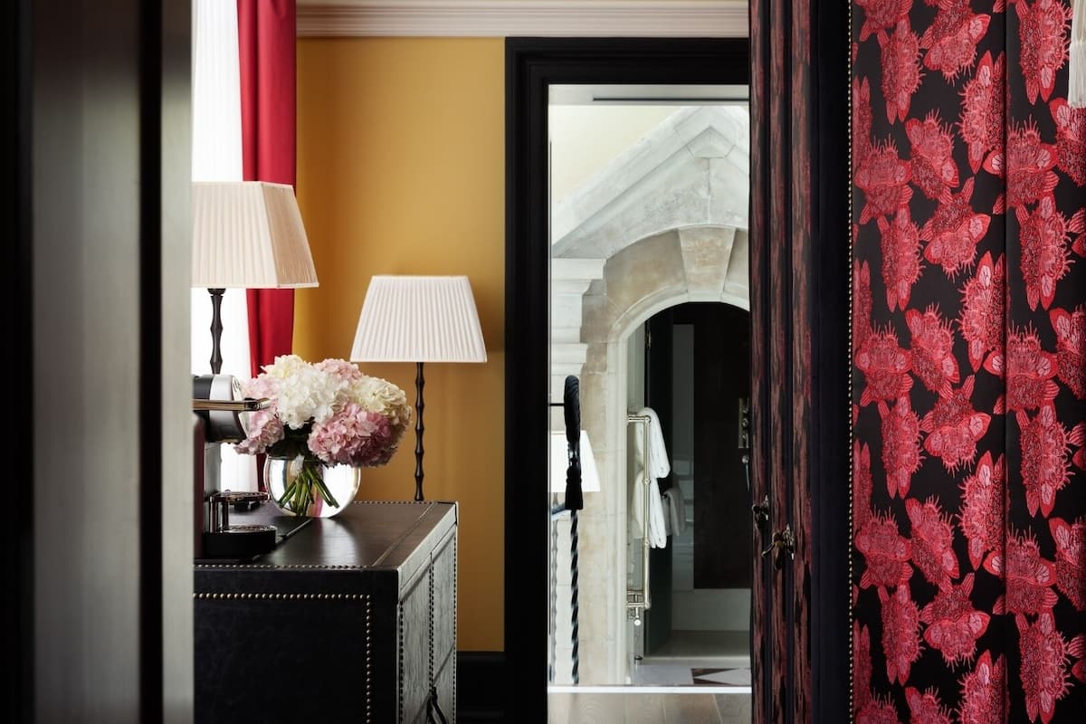 A hotel lobby with a reception desk, a vase of flowers, and a view of a stone archway.