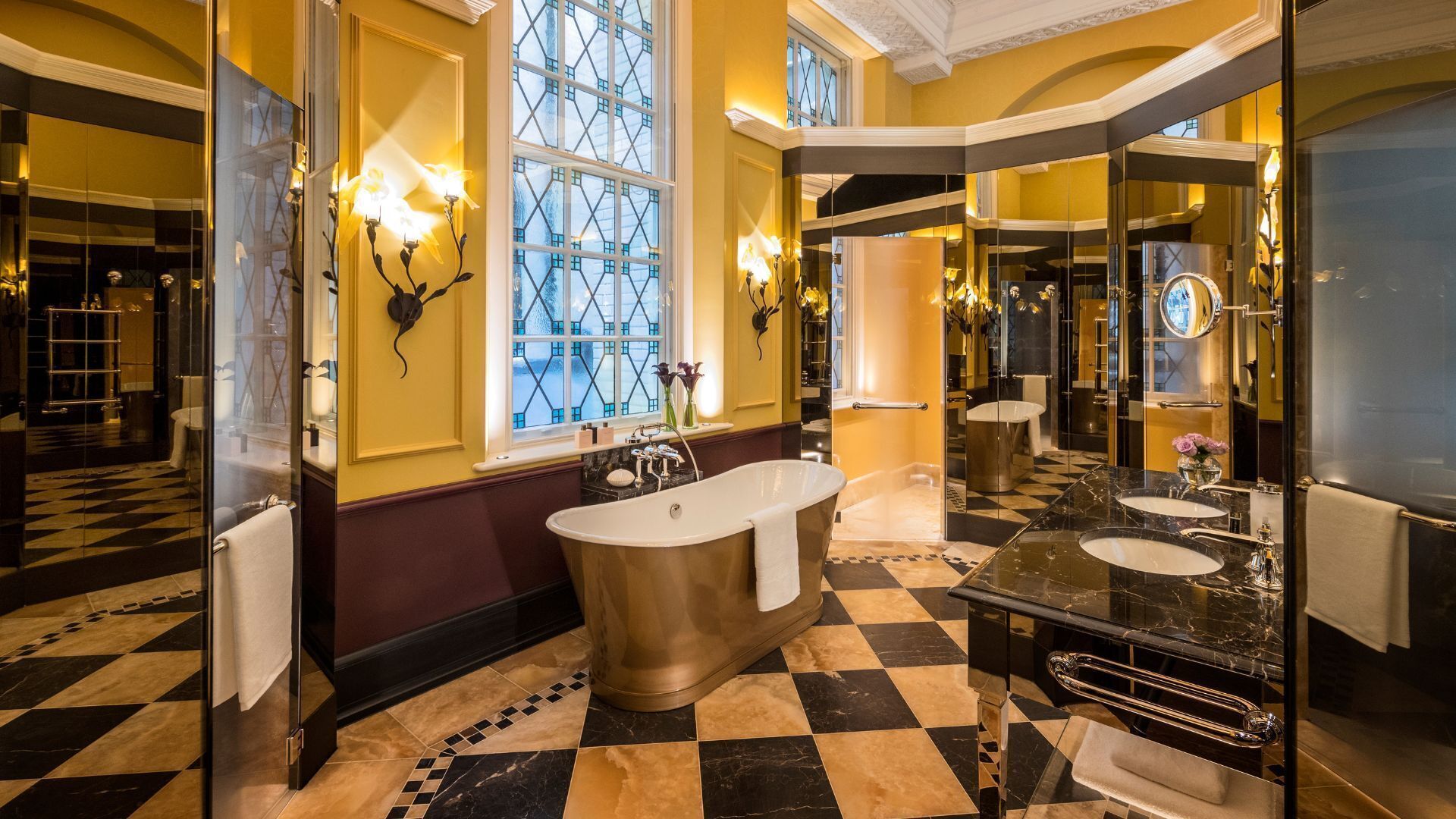 A luxurious bathroom with a freestanding bathtub, a large mirror, and a checkered floor pattern.