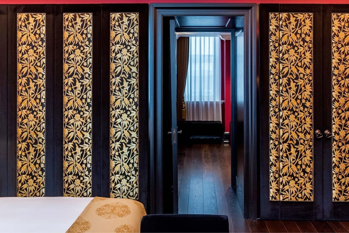 A hotel room with a bed, a desk, and a chair. There is a door leading to another room.