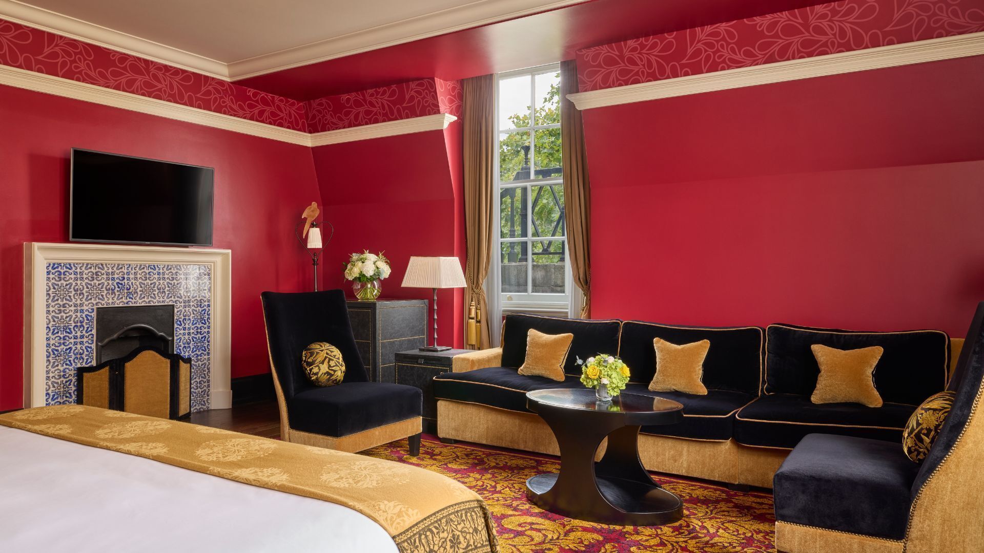 Een hotelkamer met een rode wand, een groot bed, een zithoek, een televisie en een open haard.