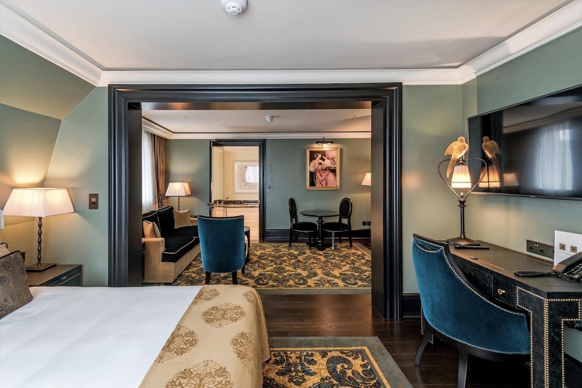A hotel room with a bed, a desk, a chair, a TV, and a painting on the wall.