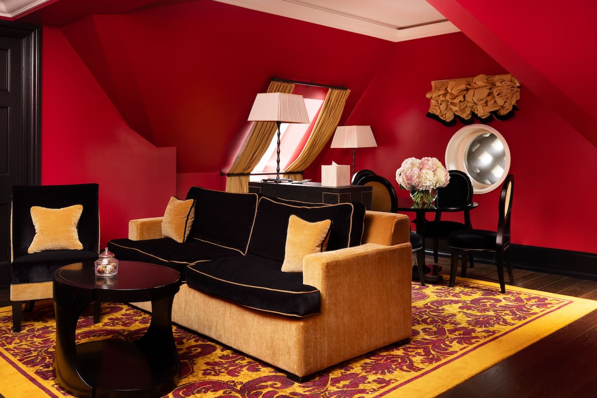 A room with a black and beige sofa, a small round table, a mirror, and a red wall.