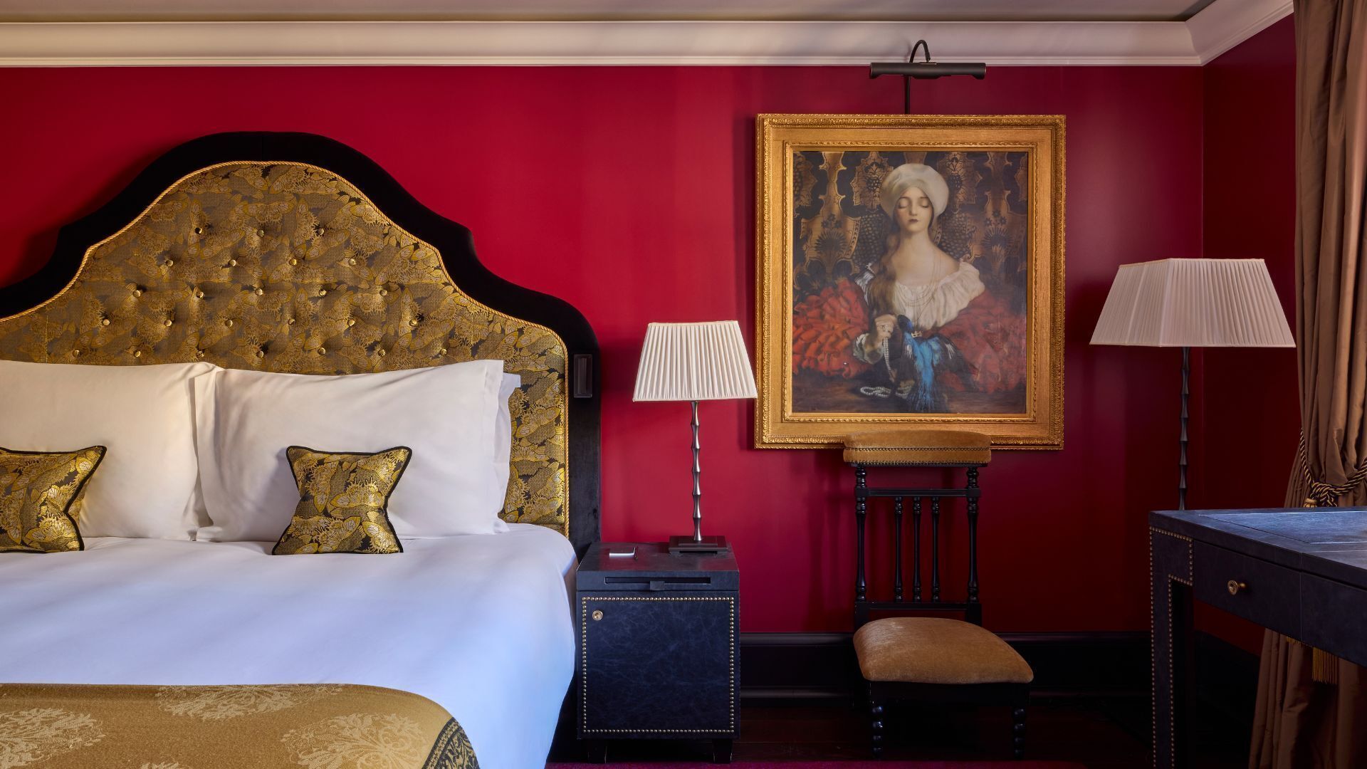 Una camera d'albergo con un letto grande, due lampade ai comodini, una scrivania e un ritratto incorniciato appeso al muro.