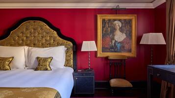 Una camera d'albergo con un letto grande, due lampade ai comodini, una scrivania e un ritratto incorniciato appeso al muro.