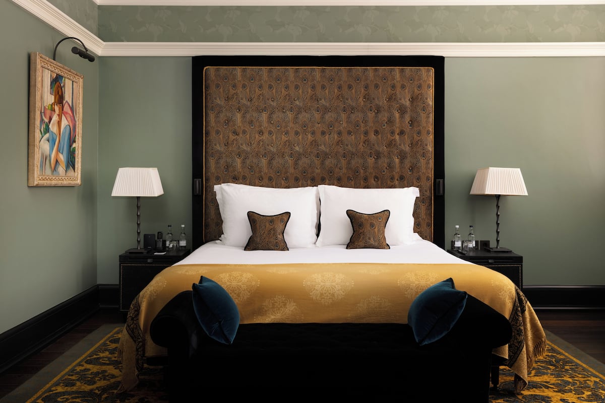 A hotel room with a large bed, two bedside tables, a painting on the wall, and a patterned carpet.