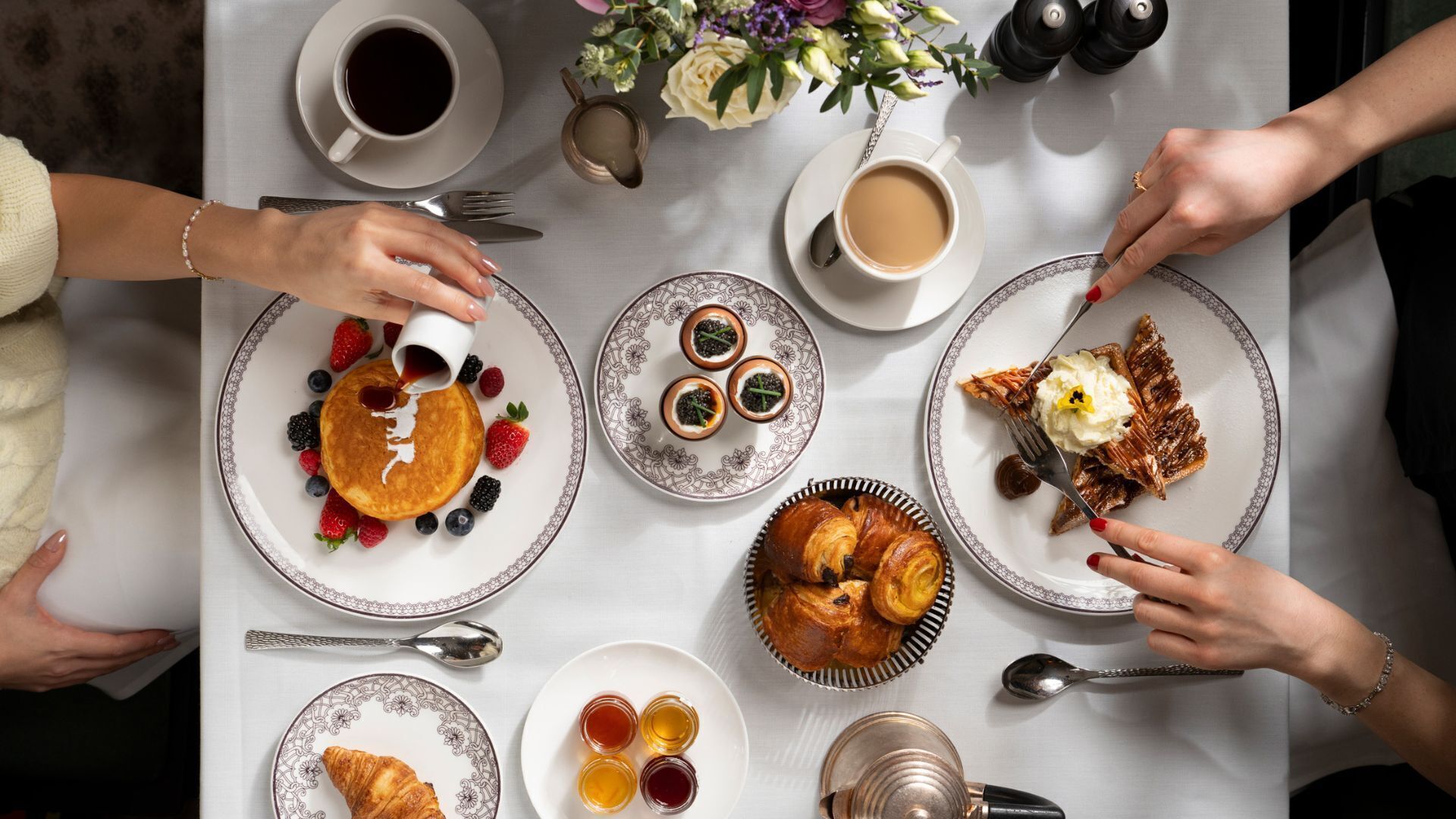 A breakfast setting with pancakes, pastries, and beverages on a table.