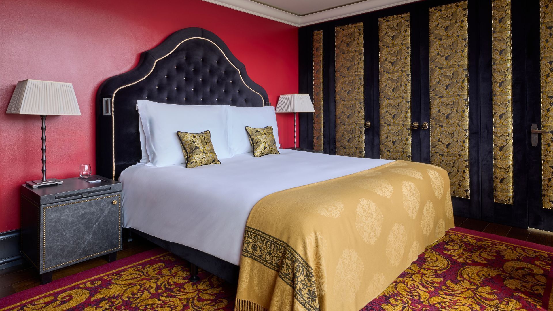 Een hotelkamer met een groot bed, twee nachtkastjes, een rode wand en een kamerbreed tapijt met dessin.