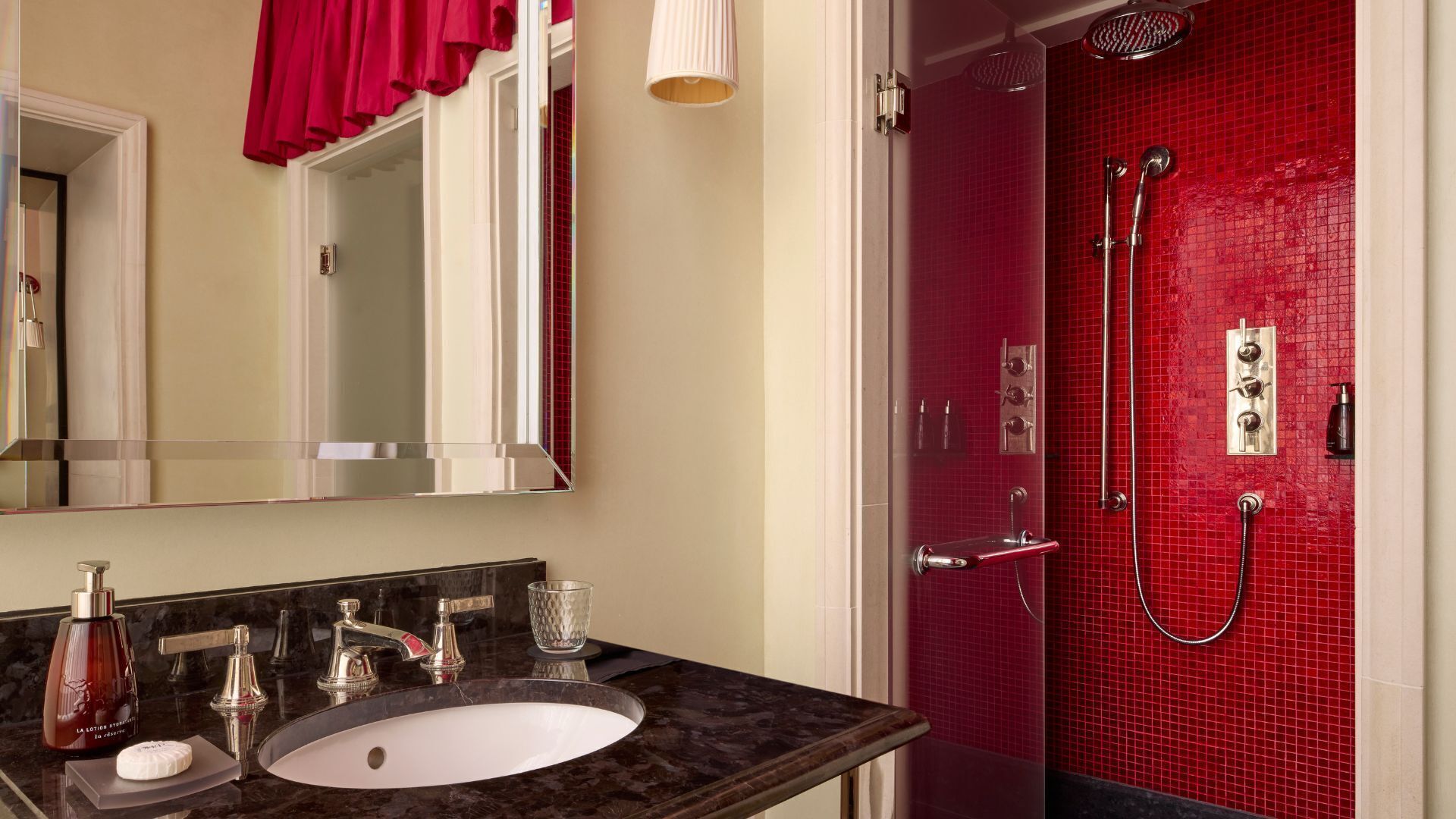 Een badkamer met een marmeren wastafel, een spiegel, een rode douchecabine en een rood gordijn.