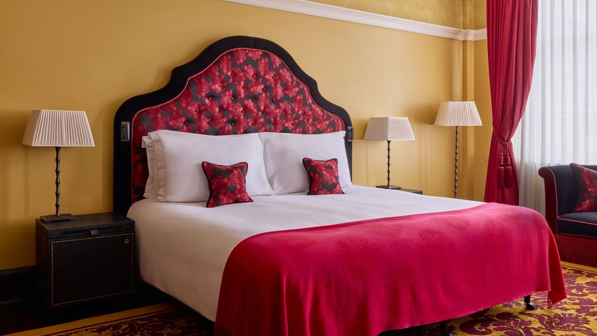 Ein Hotelzimmer mit einem großen Bett, zwei Nachttischen, zwei Lampen und einem roten Vorhang.