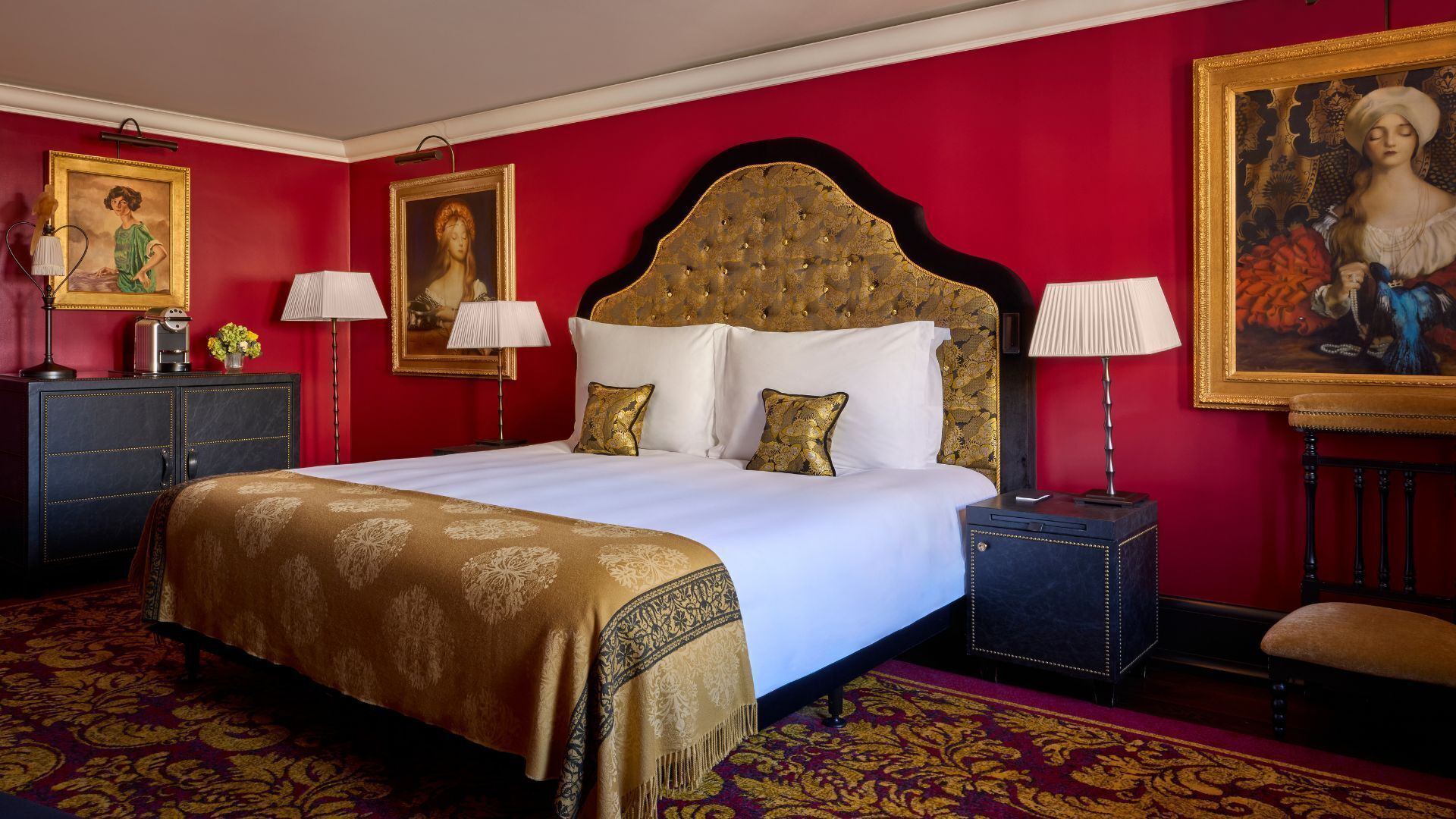 A hotel room with a large bed, two bedside tables, a nightstand, a red carpet, and two paintings on the walls.