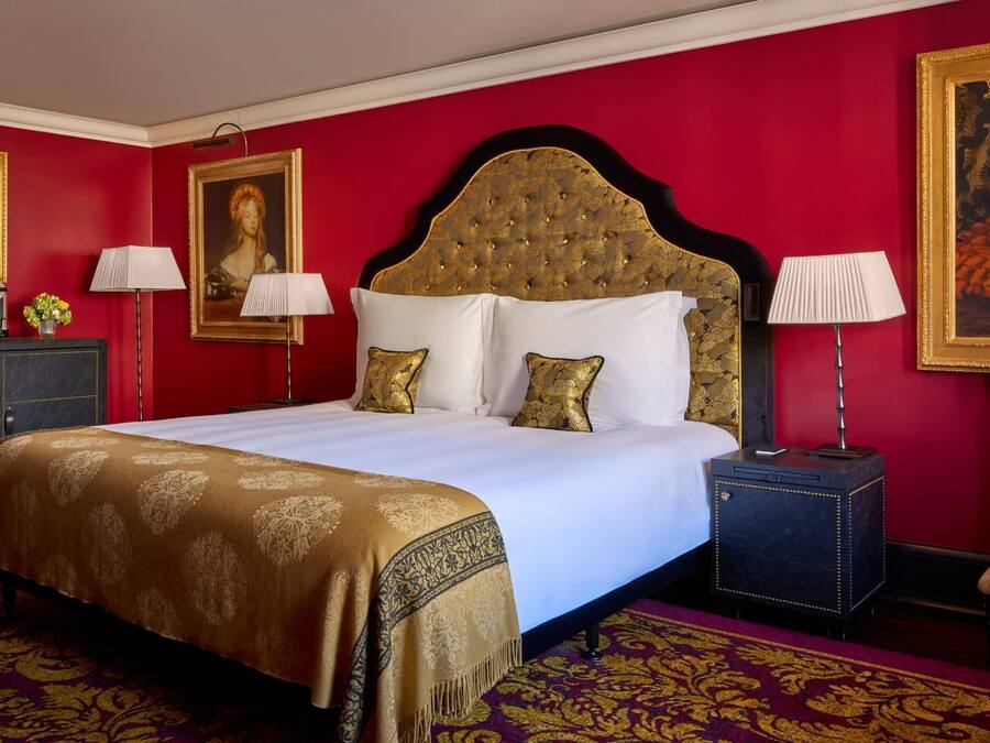 A hotel room with a large bed, two bedside tables, a nightstand, a red carpet, and two paintings on the walls.