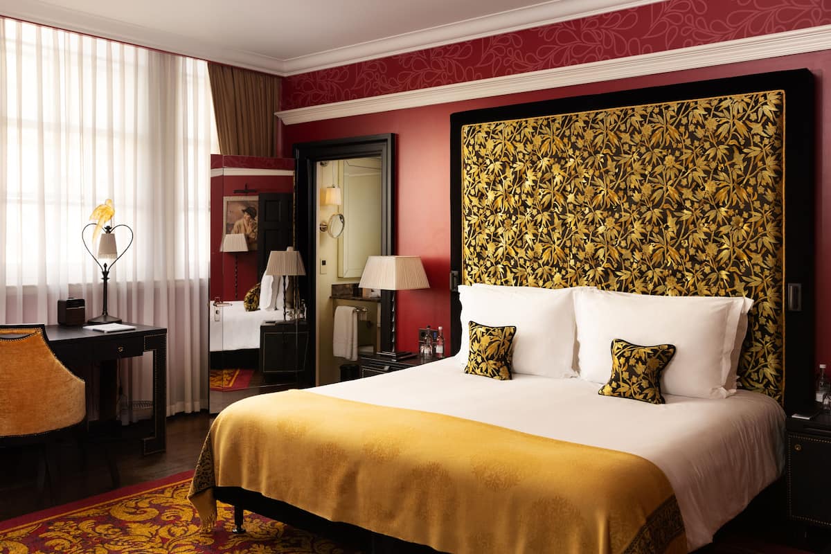 A hotel room with a large bed, a desk, a chair, a mirror, and a window with curtains.