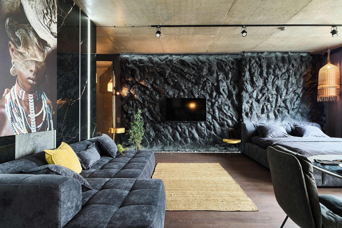 A modern bedroom with a large bed, a sofa, and a TV mounted on a textured wall.