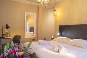 A hotel room with a large bed, a bedside table with a lamp, a mirror, and a chandelier. - The Fleece Hotel (Richmond)