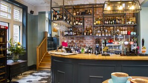 A bar area with a variety of bottles and glasses, a coffee machine, and a staircase leading to another level. - The Fleece Hotel (Richmond)