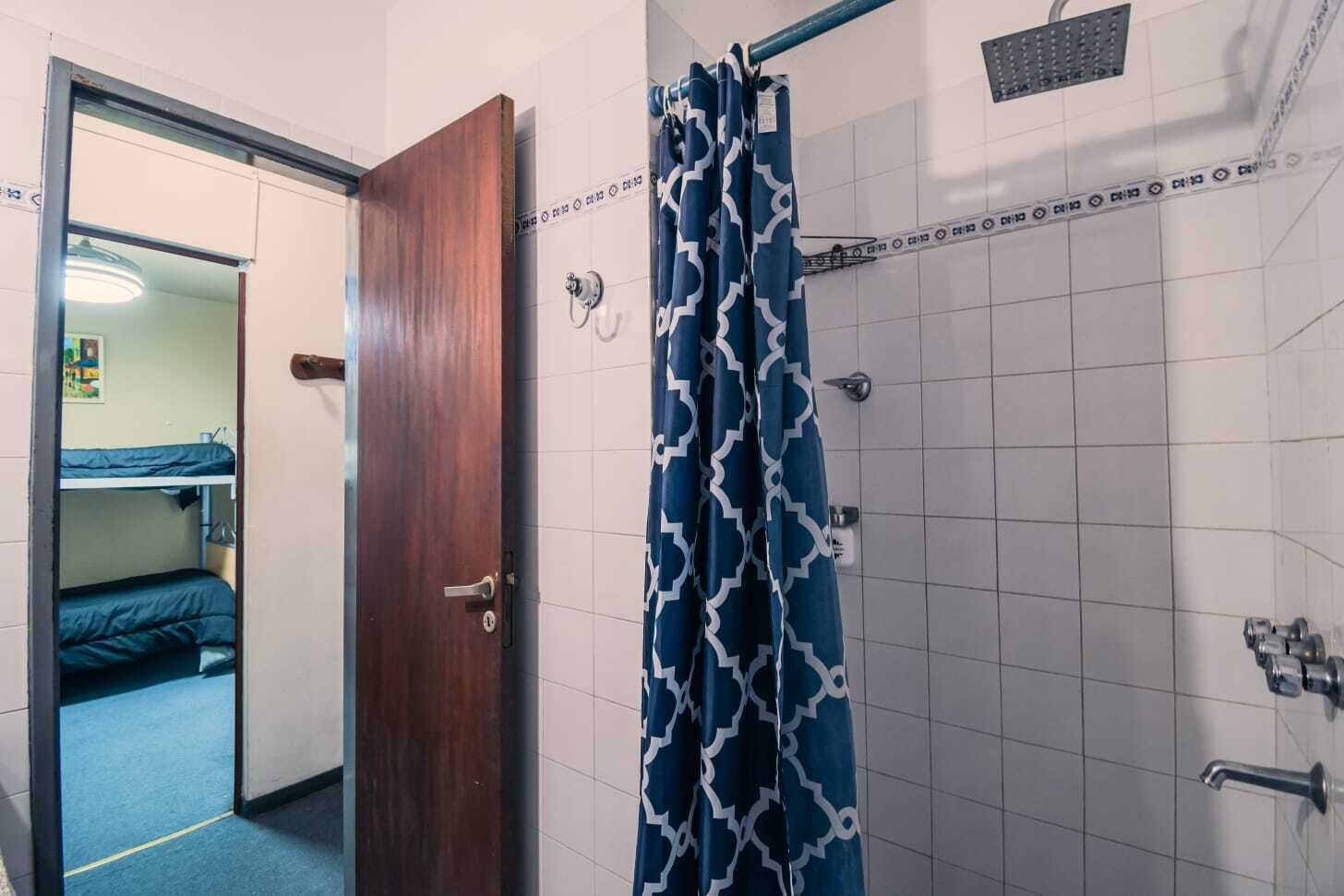 A bathroom with a shower, a door, and a visible part of a room with a bunk bed.