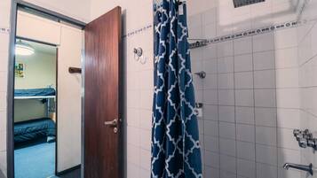 A bathroom with a shower, a door, and a visible part of a room with a bunk bed.