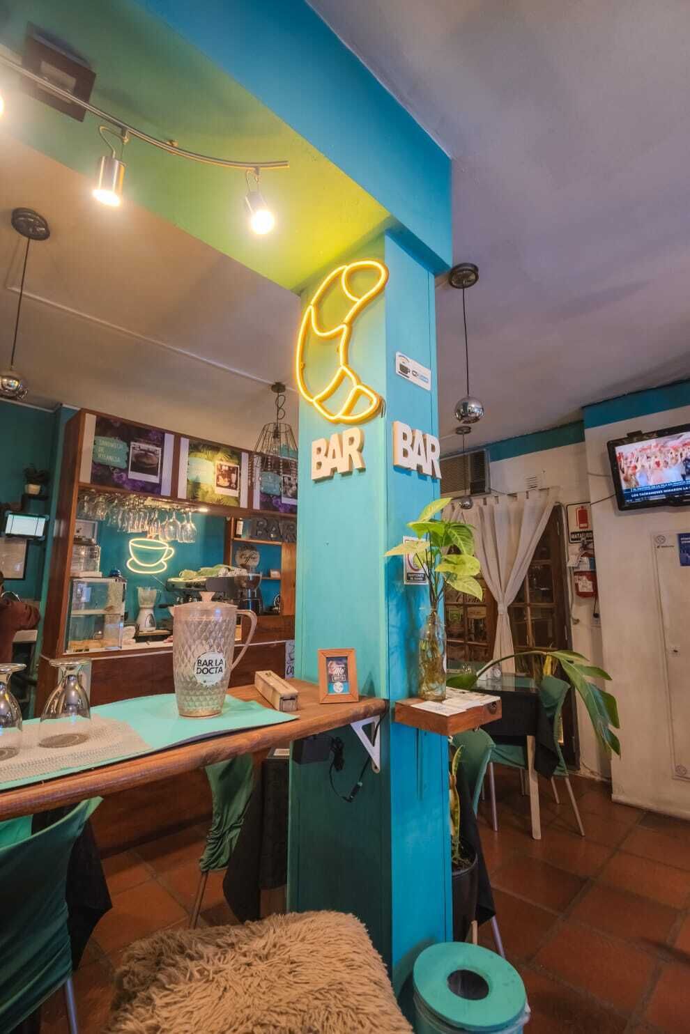 A bar area with neon signs, a television, and a plant.
