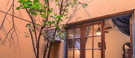 A potted tree in a courtyard with a tiled floor and a building entrance with a sliding glass door.