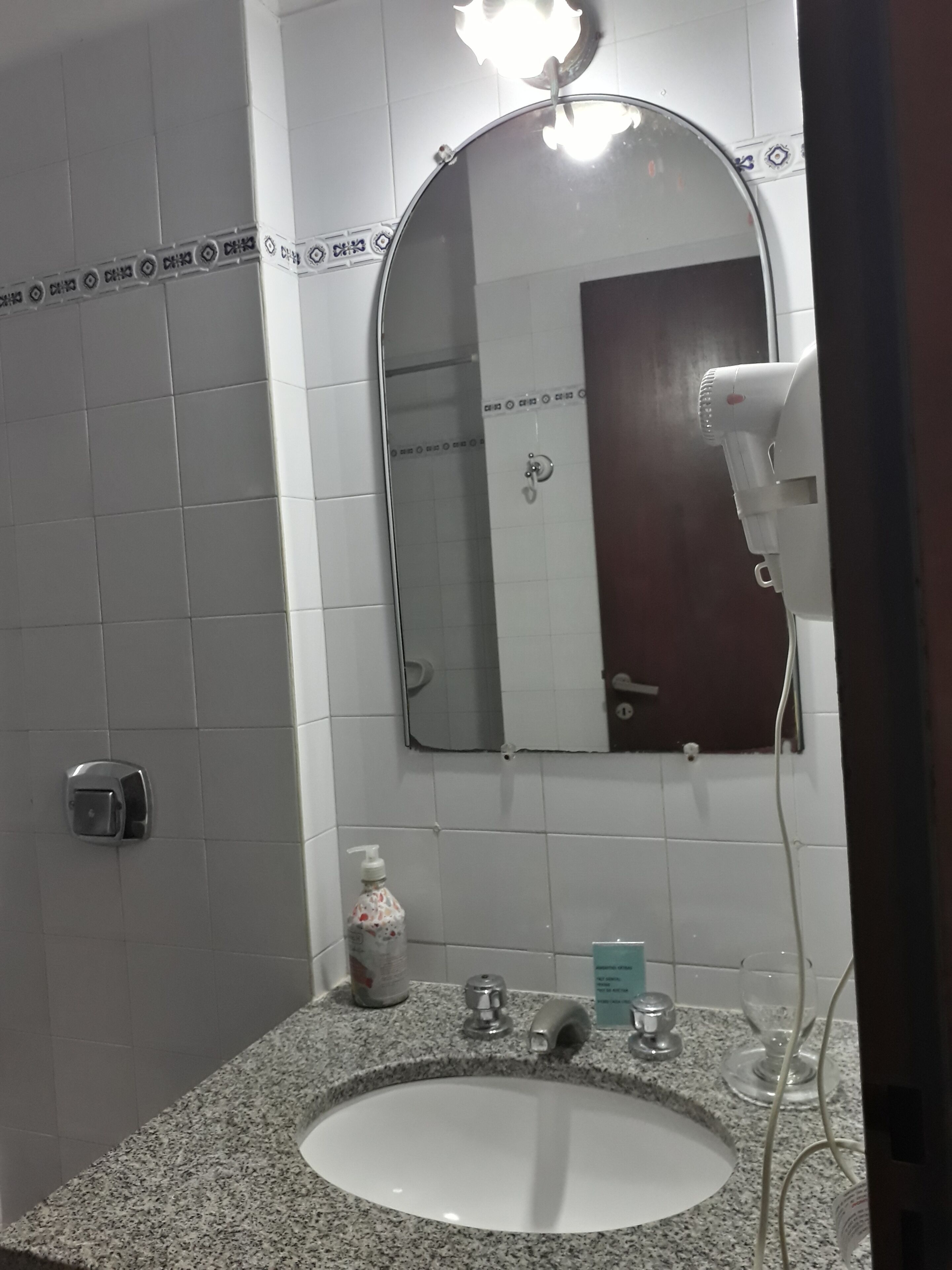 Baño con lavamanos de granito, espejo, secador de pelo y dispensador de jabón.