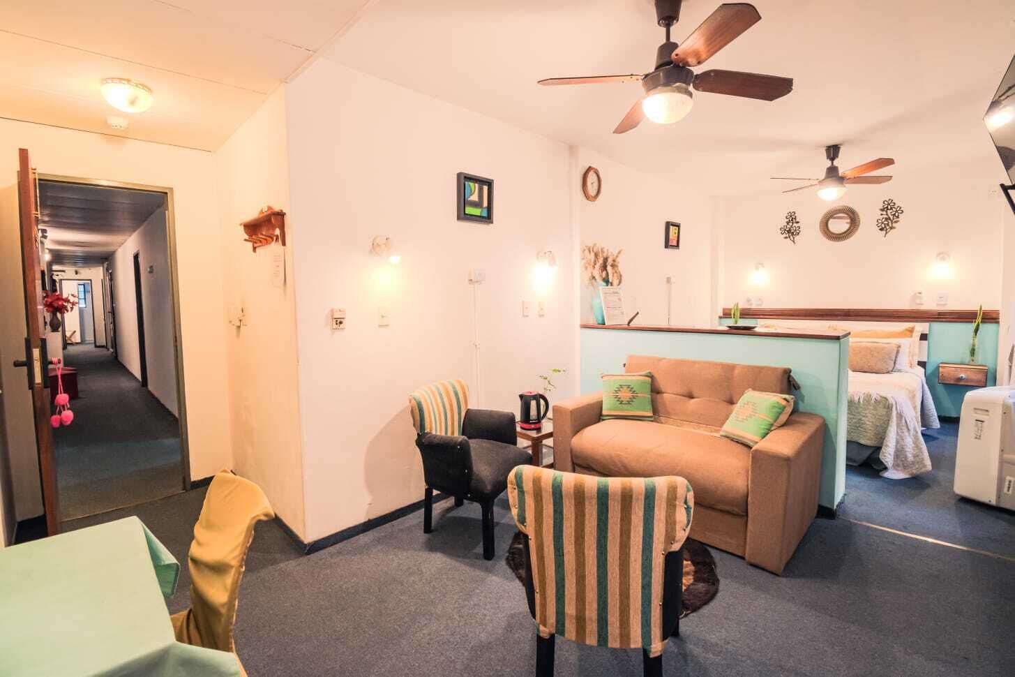 A cozy room with a sofa, chairs, a coffee table, a ceiling fan, and a bed.