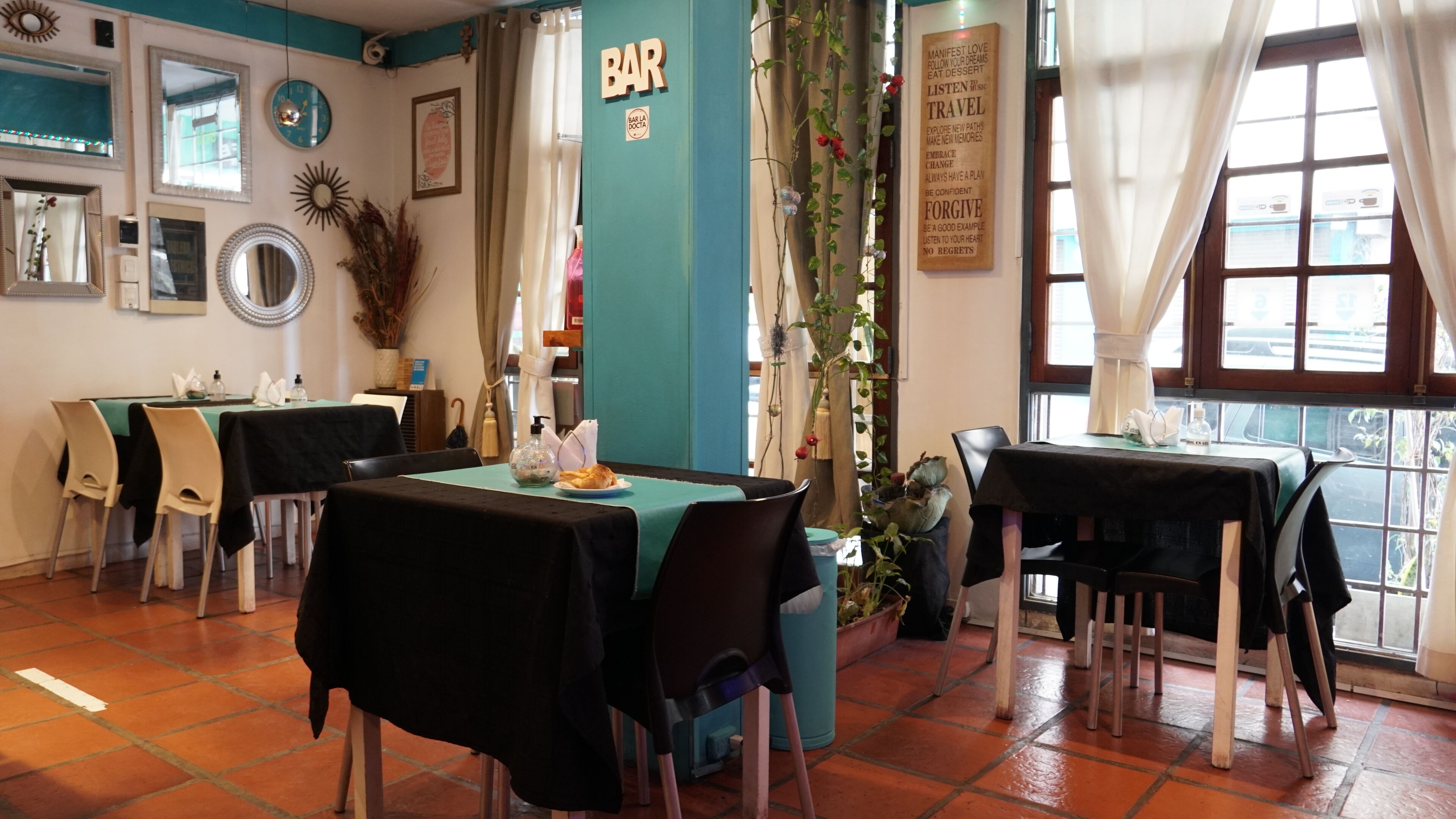 A restaurant with teal walls, a bar area, and tables set for dining.