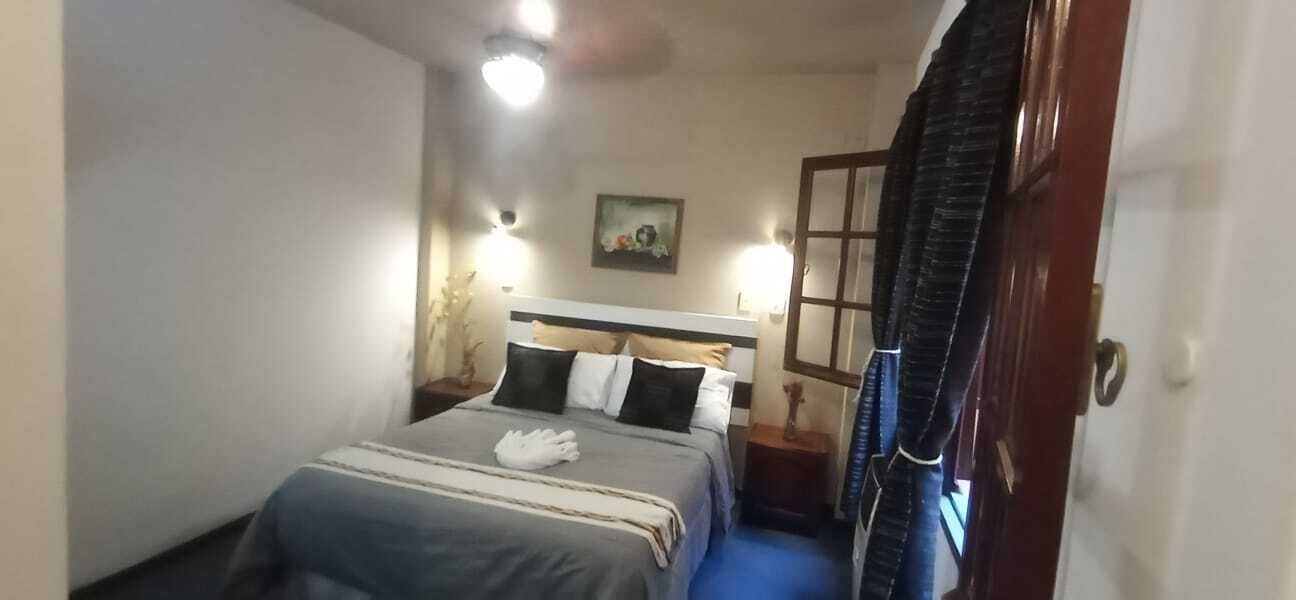 Habitación de hotel con cama, lámparas de noche, un cuadro en la pared y una puerta con cortina.