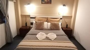 A hotel room with a bed, two bedside tables, a ceiling fan, and a painting on the wall.