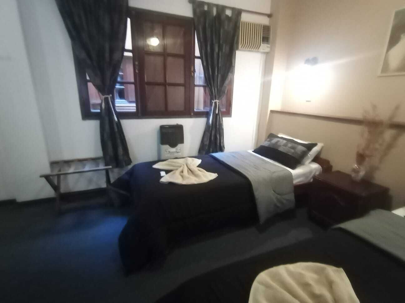 A bedroom with a bed, a bedside table, a chair, a bench, and a window with curtains.