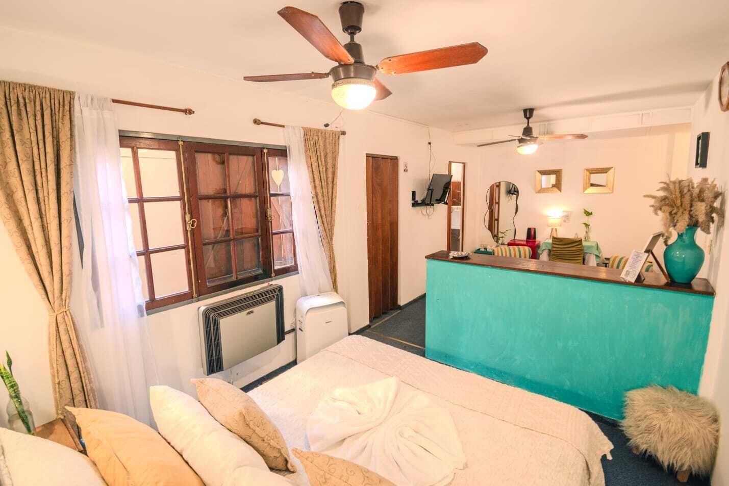 Une chambre avec un lit, un bureau, un ventilateur de plafond, un radiateur et une fenêtre avec des rideaux.