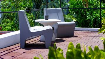 An outdoor seating area with modern furniture, surrounded by lush greenery and a metal railing.