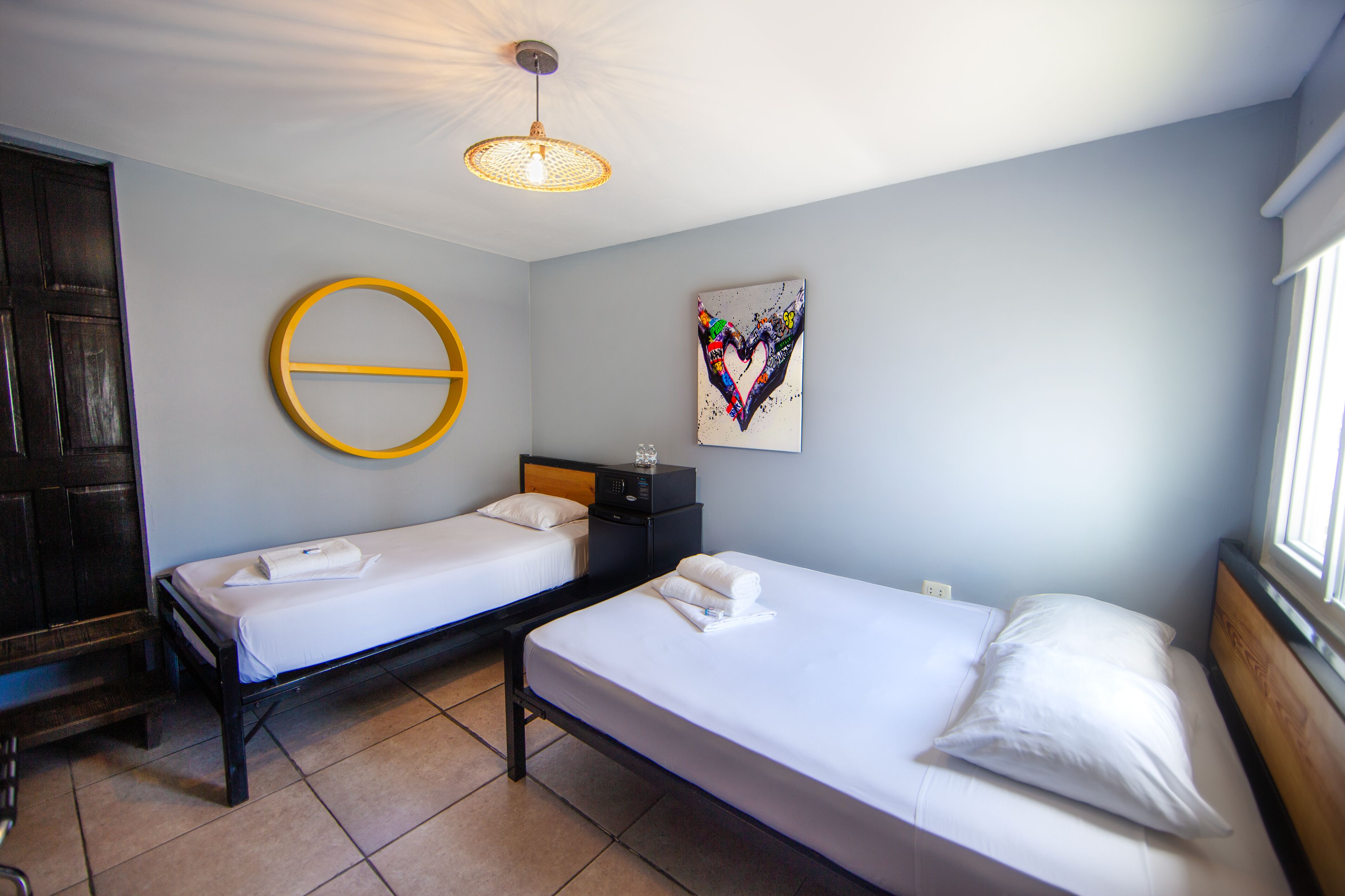 Een kamer met twee eenpersoonsbedden, een ronde wanddecoratie, een kleurrijk kunstwerk en een plafondlamp.
