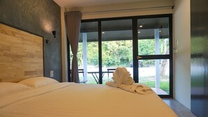 Habitación de hotel con una cama grande, cabecera de madera, ventana con cortinas y vistas a zonas verdes.