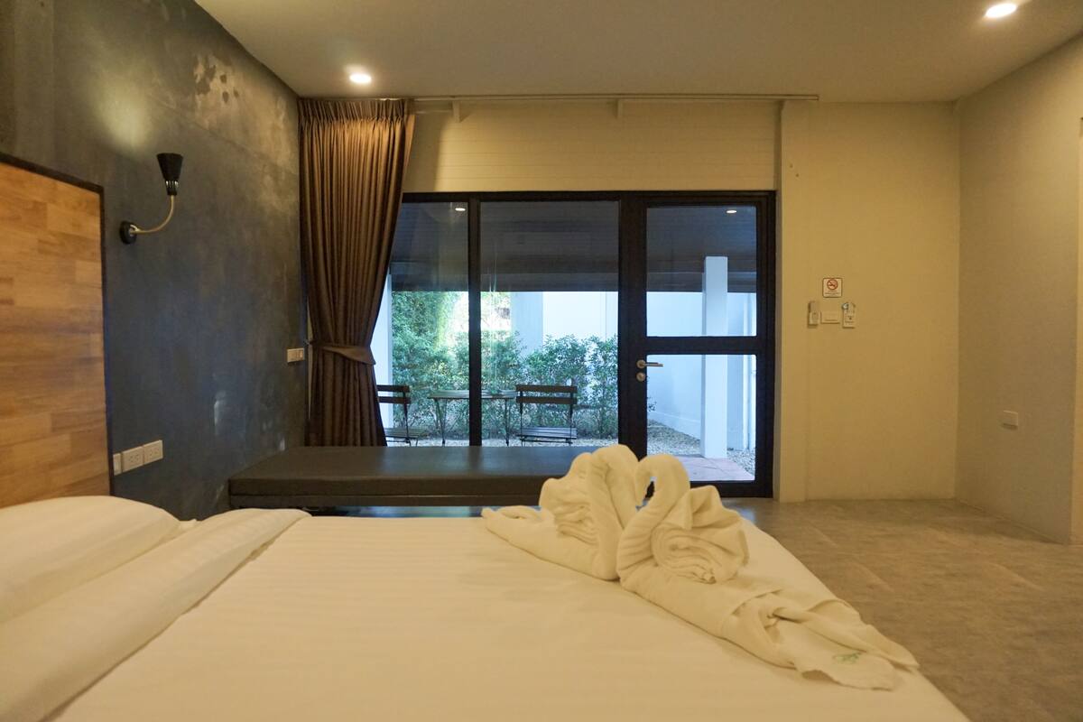 A hotel room with a bed, a bench, a view of the outdoors, and a sliding door.