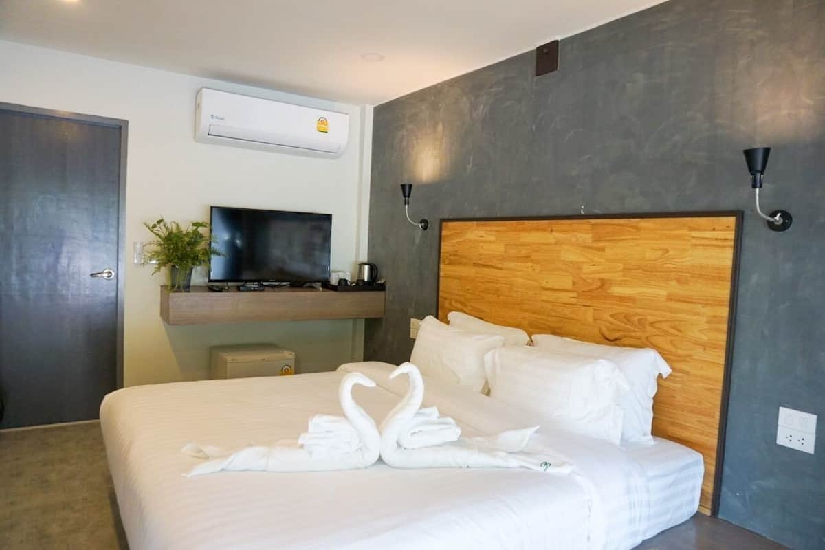 A hotel room with a large bed, a flat-screen TV, a wooden headboard, and a wall-mounted air conditioner.