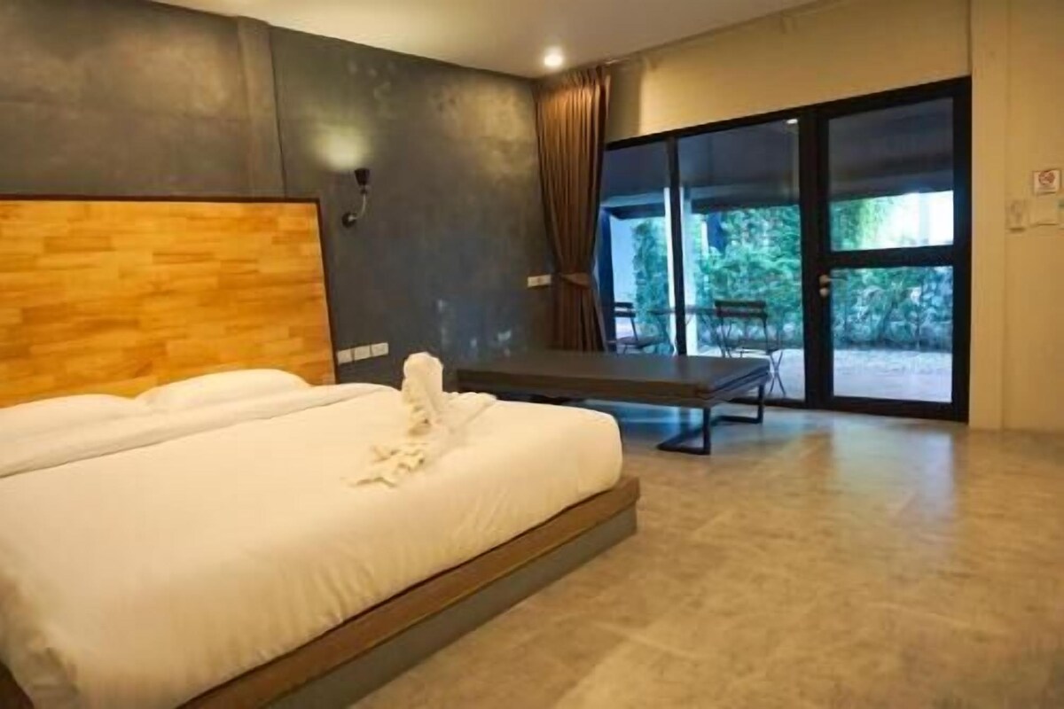 Un dormitorio moderno con una cama grande, un banco y un ventanal corredera que da a un espacio exterior.